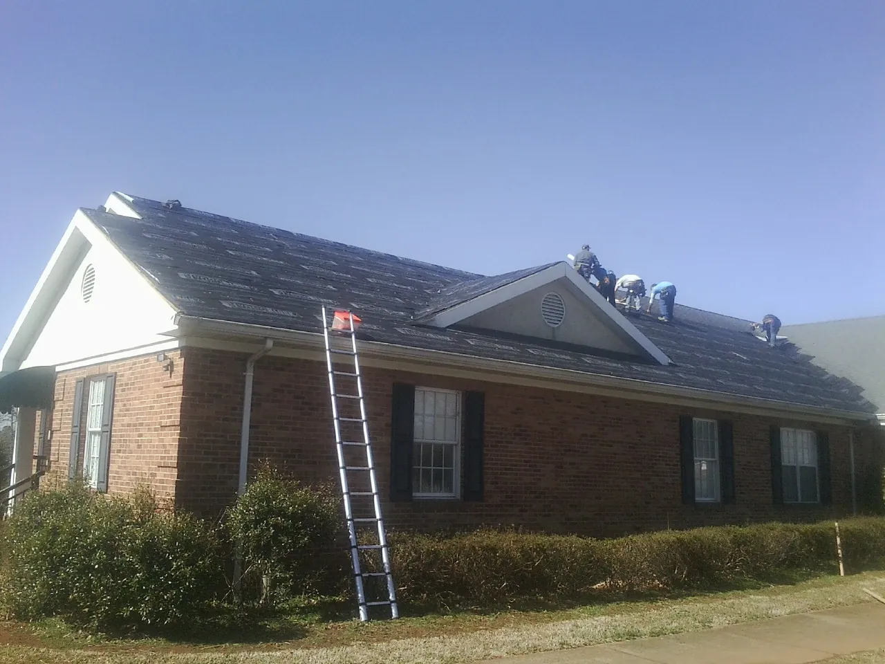 Crew tearing shingles off a brick ranch roof with a ladder set — Metal Roof Repair work by our crew in Celina